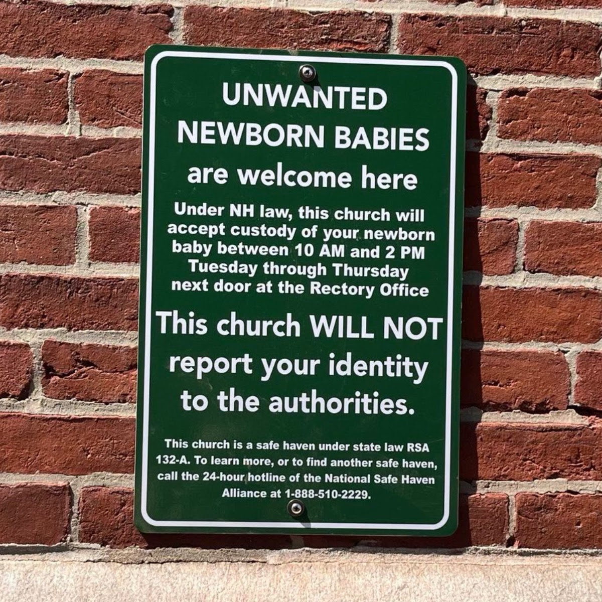The image displays a green sign on a brick wall with white text warning that the church has been designated a safe haven f...
